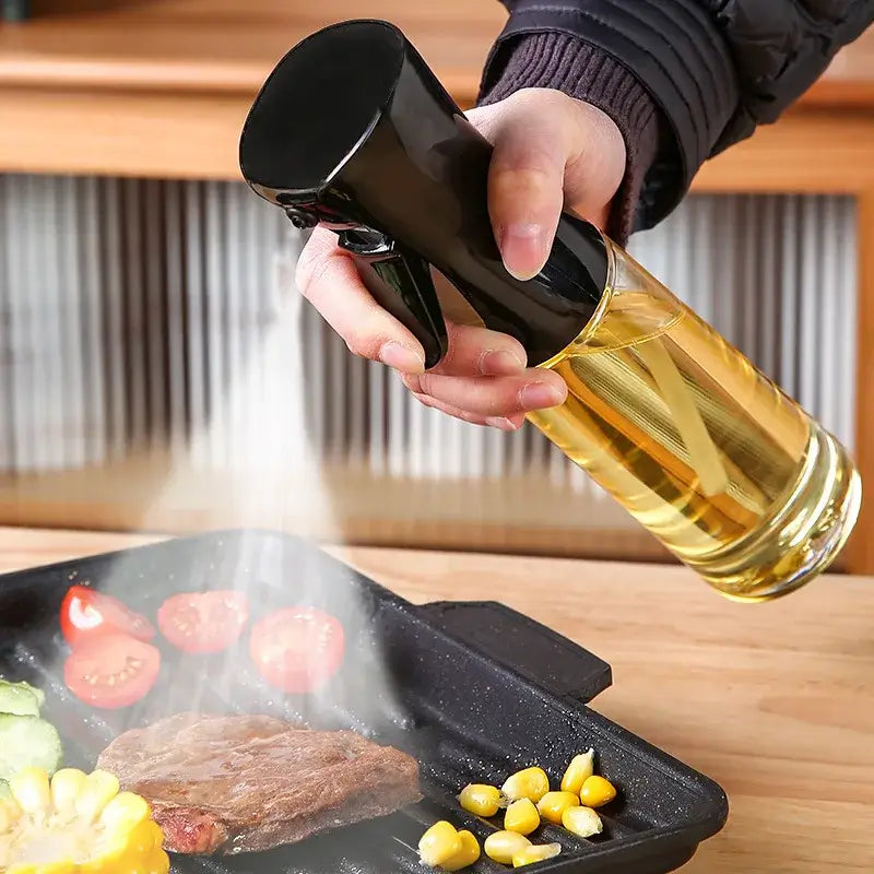 Hand spraying oil from a sleek oil spritz bottle onto grilled vegetables and steak in a pan.